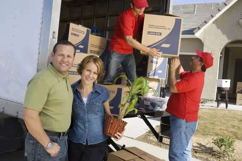 Smiling couple with movers moving boxes into a haul truck